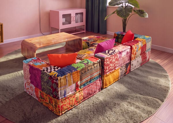 F&auml;rgglad modulsoffa i patchwork placerad runt ett soffbord i tr&auml; p&aring; en rund matta i ett modernt vardagsrum.