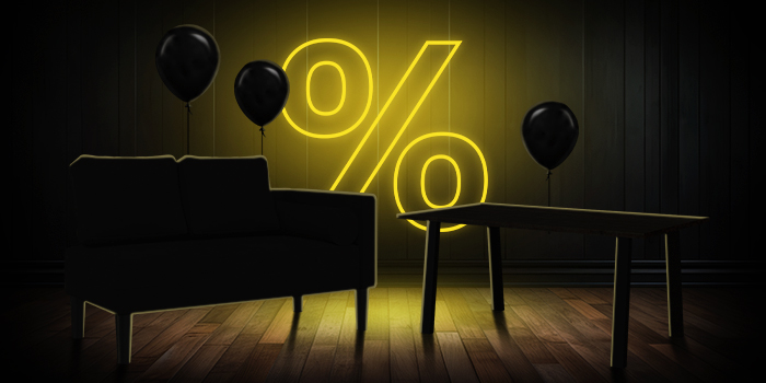 Svart soffa och träbord med svarta ballonger framför en ljust gul procentskylt på ett mörkt trägolv.